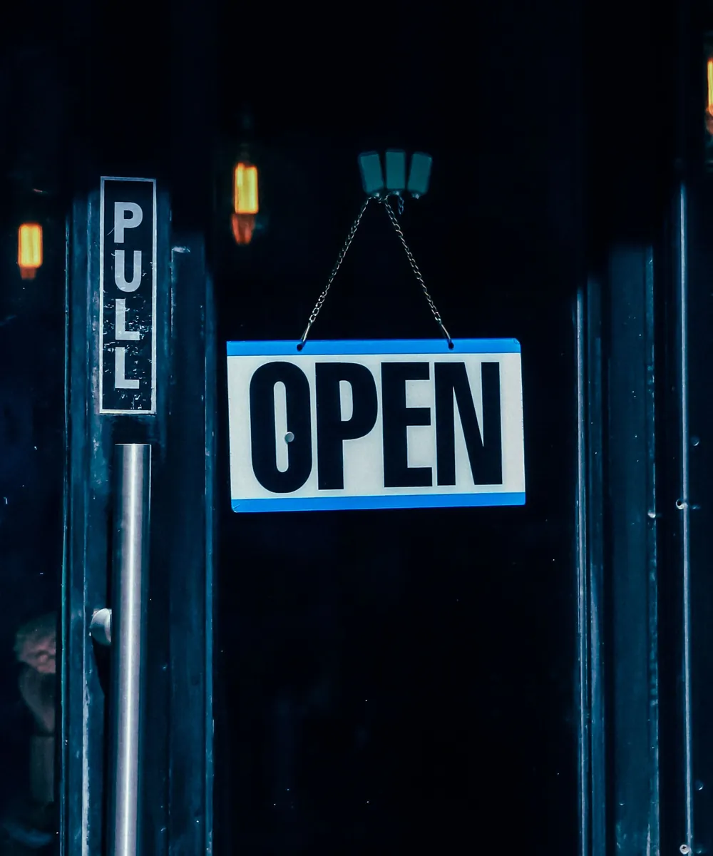 An OPEN sign hanging in the glass door of a shop, beside a PULL sign on the door handle.