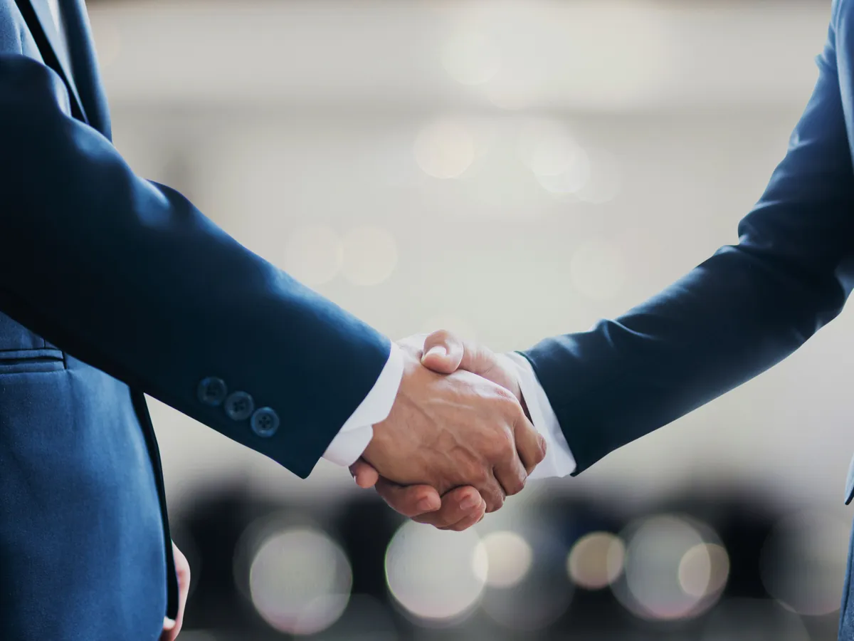 Two people in dark blue suits shaking hands.